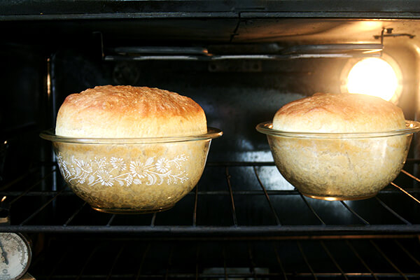 Two loaves of peasant bread baking in oven-safe glass bowls