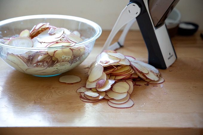Sliced potatoes on a countertop aside a mandoline.