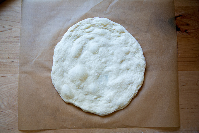 Stretched round of sourdough pizza on parchment paper.